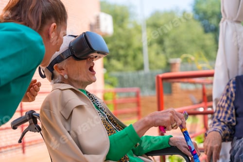 Preview: An elderly woman with the nurse looking through virtual reality glasses in the garden of a nursing