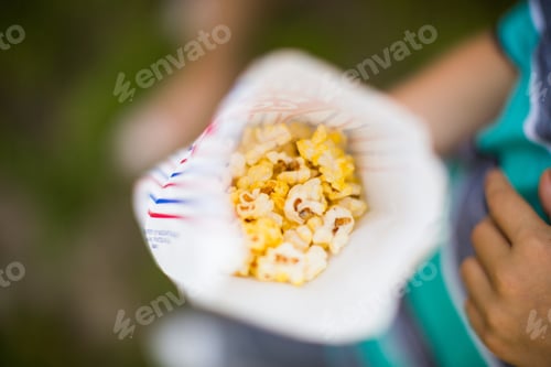 Preview: High angle shot of a person holding a paper bag with popcorn in it