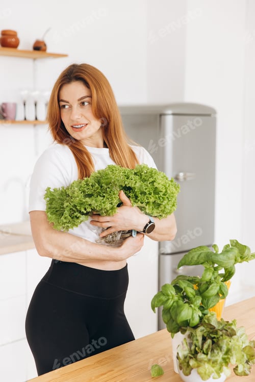 Preview: Mature sporty muscle woman in braces is holding some lettuce leaves in the home kitchen