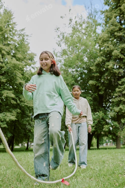 Preview: Two Preteen Girls Playing Jump Rope with School Teacher in Park Outdoors