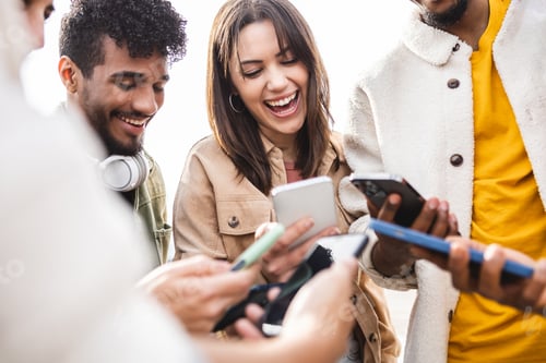 Preview: Young group of people laughing using mobile phone outdoors