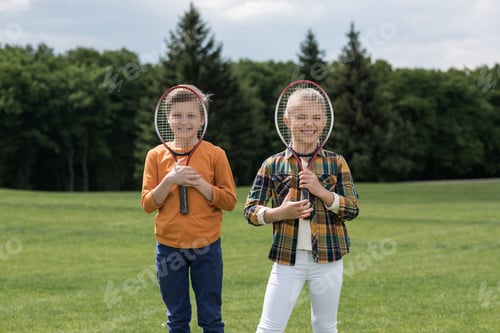 Preview: Adorable little children holding badminton racquets and smiling at camera outdoors