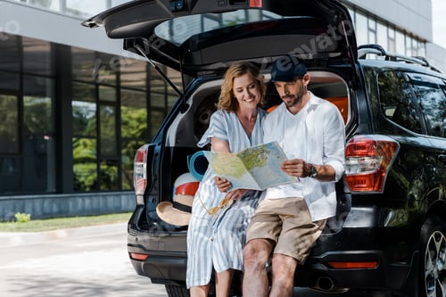Preview: cheerful man holding map near attractive woman and car