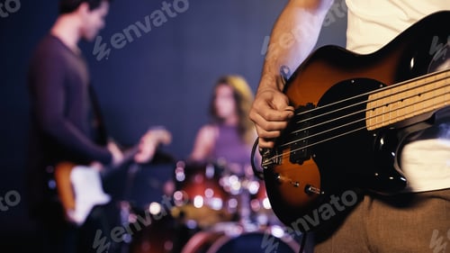 Preview: KYIV, UKRAINE - DECEMBER 30, 2021: cropped view of tattooed guitarist playing with blurred band