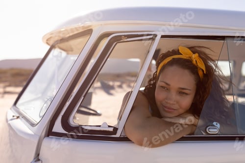 Preview: Front view of thoughtful young Mixed-race woman leaning on window of camper van at beach