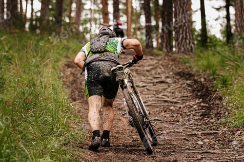Preview: dirty cyclist with mountain bike uphill