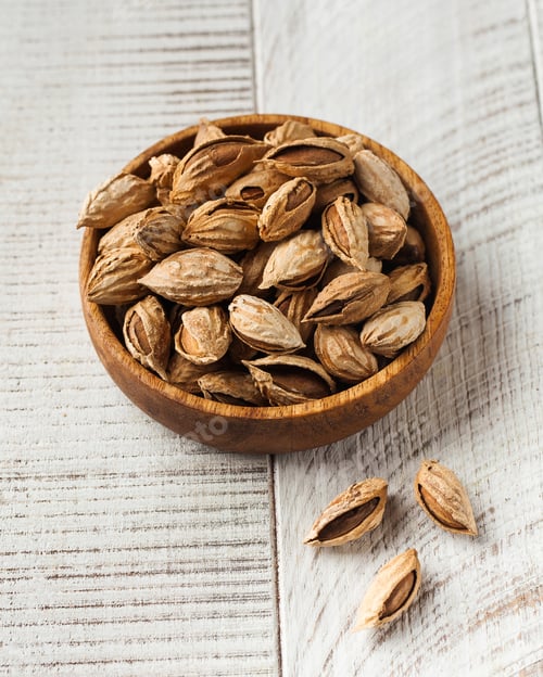Preview: Almond nuts in a shell in a wooden plate on a white wooden background. Nuts.