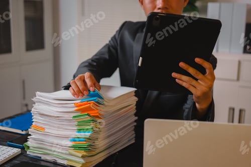 Preview: A businessman sits at his desk, working late into night on his laptop.reviews documents carefully