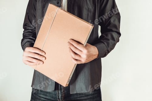Preview: Closeup shot of a man wearing a greyish shirt, standing while holding a folder on a white background