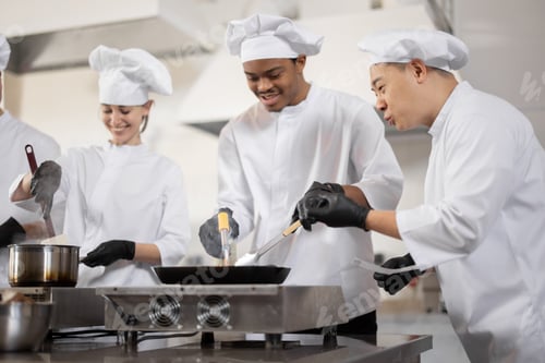 Preview: Multiracial team of professional cooks in uniform preparing meals for a restaurant in the kitchen