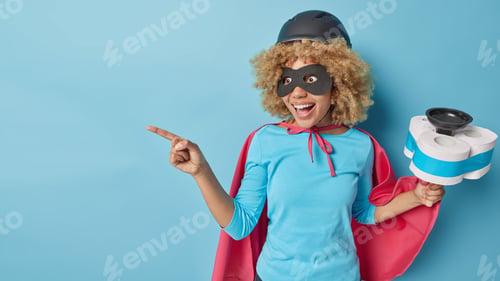 Preview: Horizontal shot of cheerful woman dressed like superhero busy doing house cleaning holds plunger wit