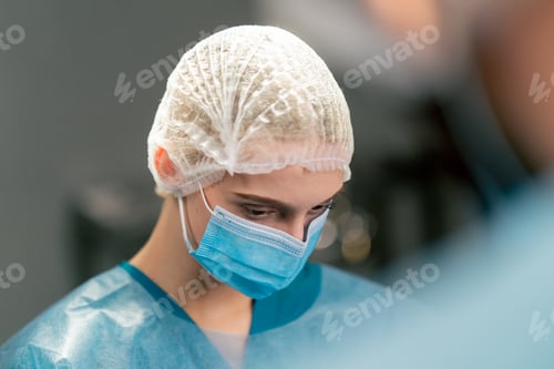 Preview: a female surgical assistant in uniform and medical mask listening attentively to her colleague