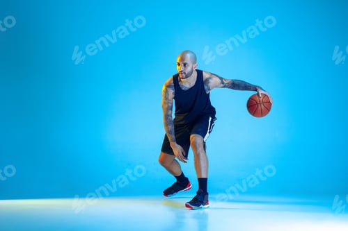 Preview: Young basketball player training isolated on blue studio background in neon light