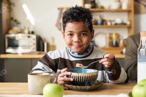 Visualização: Retrato de menino negro comendo cereal matinal e sorrindo dentro de casa