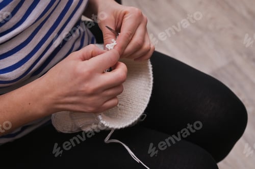 Vista previa: El gorro de bebé que se fusiona toma forma. Agujas de tejer con manos femeninas para fabricar un gorro de bebé.