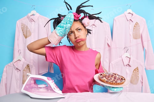 Preview: Fatigue woman tired after baking pie wipes forehead wears kitchen glove looks frustrated stands near