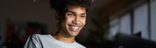 Preview: Night portrait of young smiling guy working on laptop in dark room, sitting on a