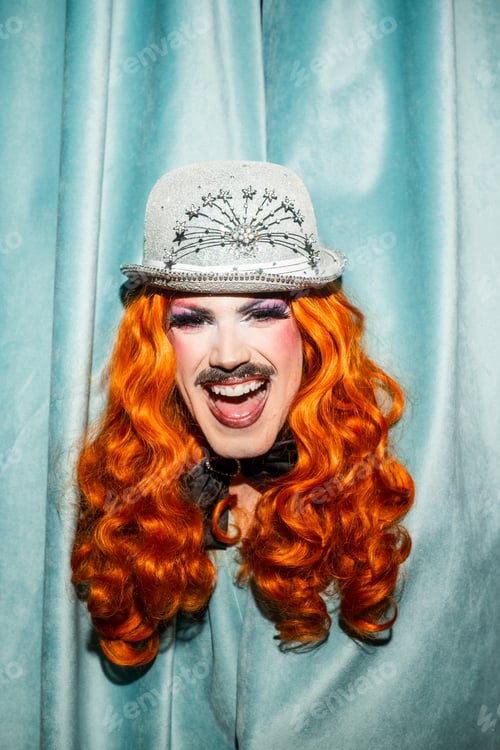 Preview: Brightly Smiling Queer Drag Performer With Orange Curls and Glittery Hat in a Fun Setting