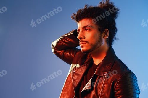 Preview: Portrait of a stylish man with curly hair on a blue background multinational, colored light, black