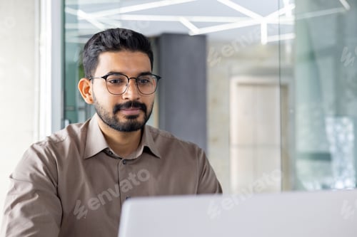 Preview: Indian businessman working on laptop in modern office