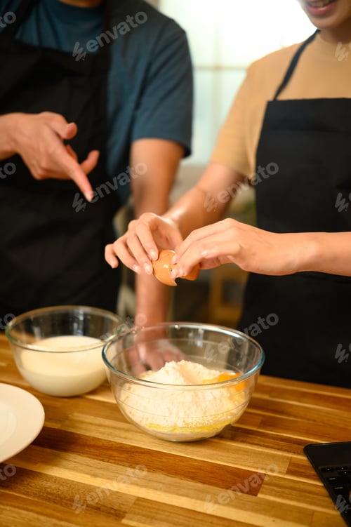 Preview: Young couple cracking egg into flour while preparing pancake batter together