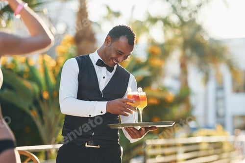 Preview: Order for woman. Black waiter in formal clothes is at his work outdoors at sunny daytime