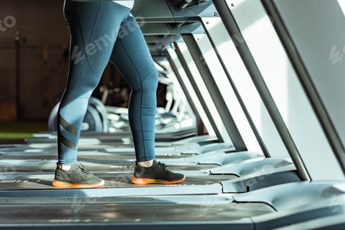 Preview: cropped view of overweight girl in leggings running on treadmill in gym
