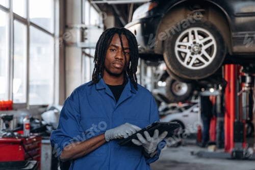 Preview: Smiling, holding digital tablet. Male mechanic is with car in garage