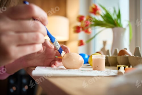Preview: Woman painting Easter egg at home with pastel paints