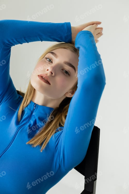 Preview: young woman with natural makeup wearing blue turtleneck while sitting with hands above head
