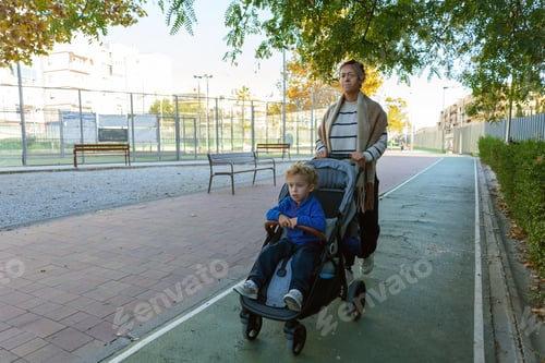 Preview: Mother pushing young child in stroller along urban park pathway, enjoying outdoor family walk