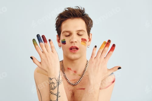 Preview: Young gay man is standing in the studio and posing for a camera. Shirtless guy with rainbow make up