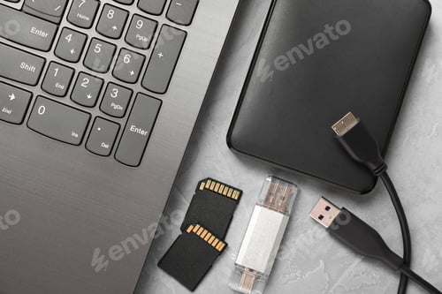 Preview: Flash drive, SD memory cards, external hard disk and laptop on gray textured table, flat lay