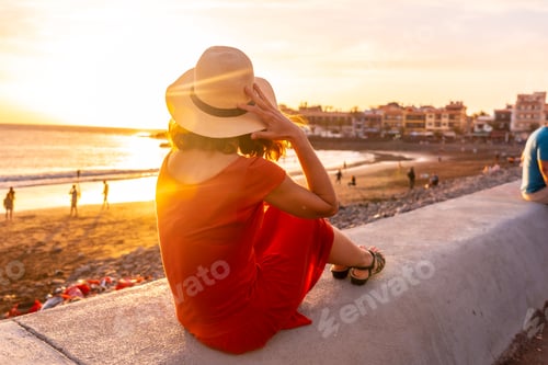 Preview: Tourist woman at sunset with a red dress on vacation on the beach of the town in La Gomera, Canary