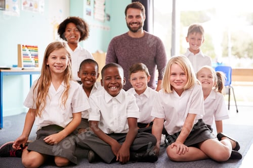 Preview: Portrait Of Elementary School Pupils Wearing Uniform Sitting On Floor In Classroom With Male Teacher