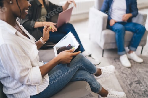 Preview: Group of anonymous multiracial colleagues sitting in armchairs and using gadgets