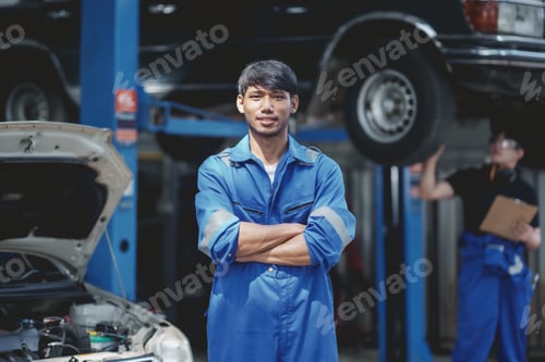 Preview: Asian man mechanic in uniform with crossed arms standing at the car repair station.