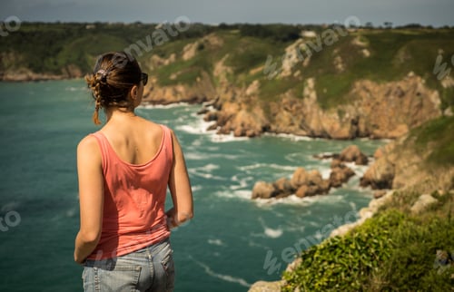 Preview: Beautiful view of a female standing on the cliffs over the ocean captured in Guernsey