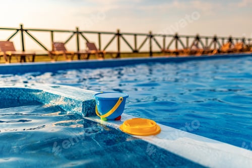Preview: A children's bucket with sieve of water and some toys are on the boat of pool against the