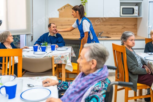 Preview: Nurse talking with senior people while eating at geriatrics