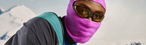 Preview: handsome young man in pink balaclava with sunglasses with snowy backdrop, winter concept, banner