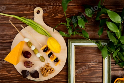 Preview: top view of cheese set as cheddar and parmesan with olive, walnut, grape and flower on cutting board