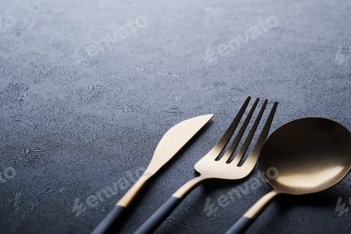 Preview: Gold spoon, fork, knife and clean empty black plate. Set of stylish black and gold cutlery on black
