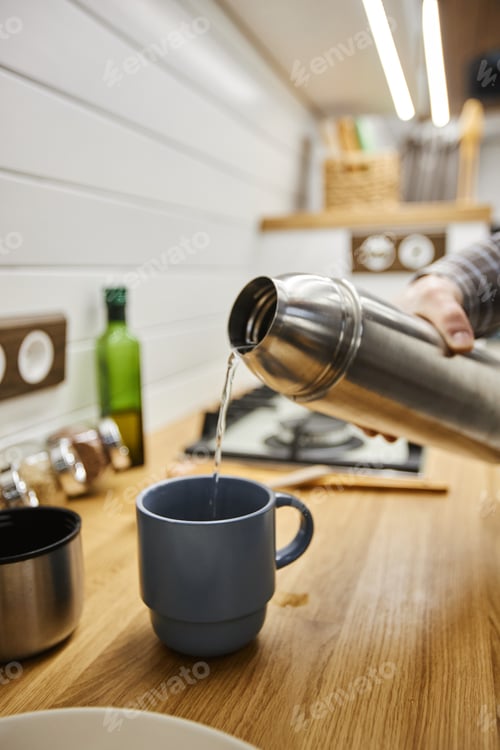 Preview: Young man pouring hot coffee into cup from thermos travelling with trailer van