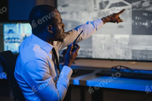 Preview: African-American security officer watching the screens talking on radio in control room