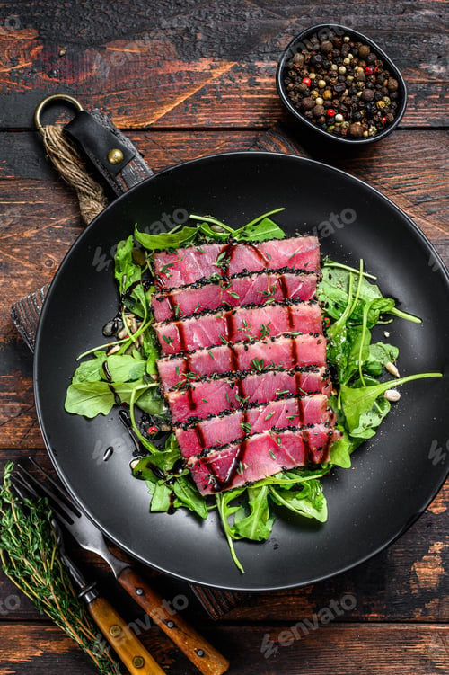Preview: Grilled teriyaki Tuna steak salad with arugula and spinach. Dark wooden background. Top view