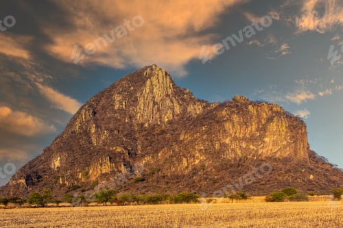 Preview: Beautiful view of a giant rocky cliff on a grassy field under a cloudy sky