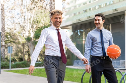 Preview: Two business colleagues walking and laughing outdoors while holding a basketball