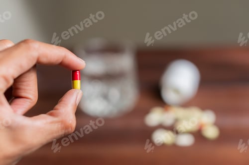 Preview: Hand Holding Pills with Syringe on Wooden Surface