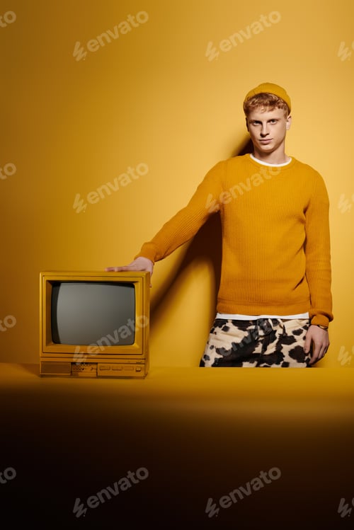Preview: A stylish young man with red hair stands by a vintage TV in a winter outfit.